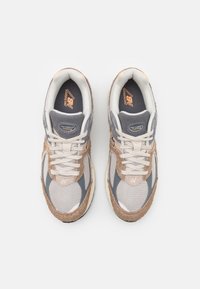 Ruskeat ja harmaat tennarit, joissa verkko- ja mokkanahkaiset materiaalit. Niissä on valkoiset nauhat, pehmustettu kaulus ja oranssi logo kielen kohdalla.