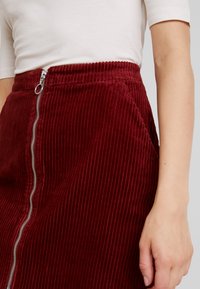 Burgundy khakiskor med vertikala ränder, med en silverfärgad sidokjol och en strukturerad, ribbad finish.