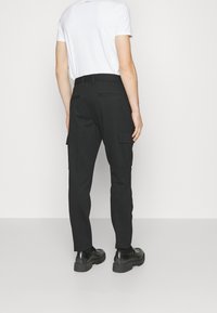 Mustat cargo-housut slim fit -mallissa, joissa on sivutaskut, vyölenkit ja sileä kangas. Yhdistetty valkoiseen t-paitaan ja mustiin kenkiin.