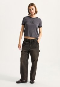Grå cropped t-shirt med sorte accenter og grafisk print, parret med løstsiddende mørke denimbukser med lige snit og flagrende kanter.