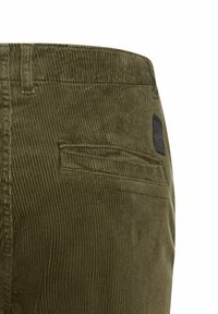 Olive green corduroy pants featuring a back pocket and a black logo patch. The fabric has vertical ridges and a soft texture.