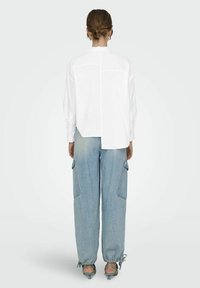 Camicia bianca a maniche lunghe, fit largo, con orlo asimmetrico. Abbinata a jeans baggy blu chiaro con tasche cargo e polsini con coulisse.