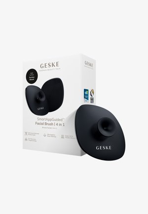 Spazzola viso smart nera GESKE 4-in-1 con montaggio a ventosa mostrata accanto alla confezione bianca del prodotto con loghi dei premi e benefici di pulizia.