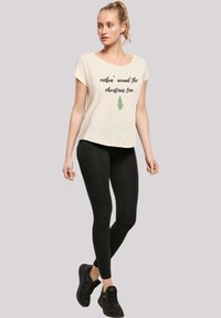 Cremefarbene Baumwoll-T-Shirt mit "rockin' around the Christmas tree" in Schwarz gedruckt, mit einer grünen Baumgrafik. Kombiniert mit schwarzen Leggings und Turnschuhen.