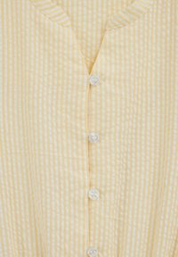 Tissu rayé jaune et blanc avec un col en V et cinq boutons sur le devant ; matière douce et texturée avec des coutures visibles.