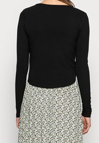 Black ribbed long-sleeve top with a rounded neckline, paired with a floral-patterned skirt featuring a mint green background and black accents.