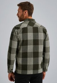 Chemise à carreaux verte et blanche avec un tissu texturé, manches longues et col. Elle dispose de poignets à boutons et de détails aux épaules.