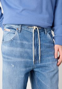 Svijetloplave traperice s rastezljivim vezanjem, vidljivim izblijedjenjem i suptilnim oštećenjima sprijeda. Calvin Klein logo na džepu.