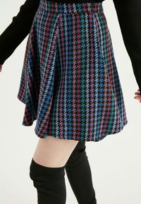 Rocková sukně s houndstooth vzorem v modré, červené, zelené a černé barvě. Vyrobena z texturované látky s přiléhavým pasem a sklady.