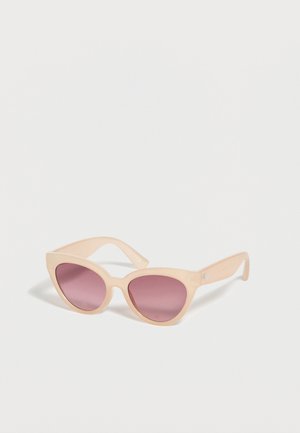 Lunettes de soleil œil-de-chat avec des montures beiges et des verres dégradés violets posées sur une surface blanche.