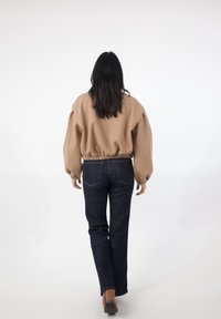 Brauner, übergroßer Pullover mit geraffter Taille, kombiniert mit dunkelblauen Jeans. Der Pullover hat ballonartige Ärmel und gerippte Bündchen.