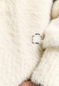 White fluffy textile with a soft texture, featuring a silver metal accent in an arch shape. Close-up view emphasizes the fabric's fibers.