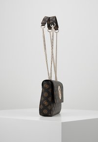 Sac à main noir à motifs avec une forme structurée, doté d'un rabat avant, d'une quincaillerie en or et de deux bandoulières en chaîne pour plus de polyvalence.