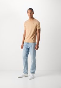 Camiseta de manga corta beige con escote redondo, combinada con jeans rectos de color azul claro y zapatillas blancas. Diseño simple y limpio.