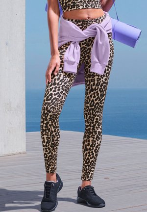 Leopard print leggings with a high waist, made of stretch fabric, paired with a lavender sweatshirt tied at the waist and black athletic shoes.