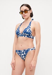 Kék és fehér bikini szett, háromszög alakú toppal és alacsony derekú bugyival, merész absztrakt grafikai mintával. Simogató, puha tapintású anyag.