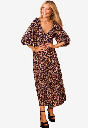 Leopardenmuster-Kleid mit V-Ausschnitt, Puffärmeln und fließender Silhouette in Braun-, Schwarz- und Blautönen. Zu den schwarzen Absätzen getragen.