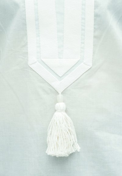 Λευκό βαμβακερό ύφασμα με υφή και ντεκολτέ σε σχήμα V, με κρεμαστή φούντα με κρόσσια κεντραρισμένη κάτω από την περιοχή του γιακά.