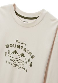 T-shirt en coton rose clair avec un col rond, présentant un graphique de montagne verte et le texte "Les Montagnes Jumelles Explorez Plus" imprimé sur le devant.