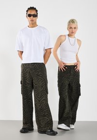 Cargo pants in dark green with a zebra stripe pattern, featuring side pockets; paired with a cropped white t-shirt and a fitted white tank top.