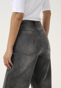 Gray denim pants with a high waist, five-pocket design, and subtle distressed texture. Back pockets feature a classic shape.