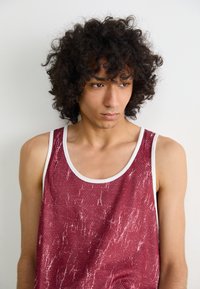 Débardeur rouge avec un design texturé et des accents blancs. Le matériau semble respirant et présente un motif de stries subtiles.