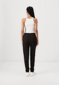 Black and brown striped jogger pants, elastic waistband, paired with a white tank top. Back view focuses on relaxed fit and texture.