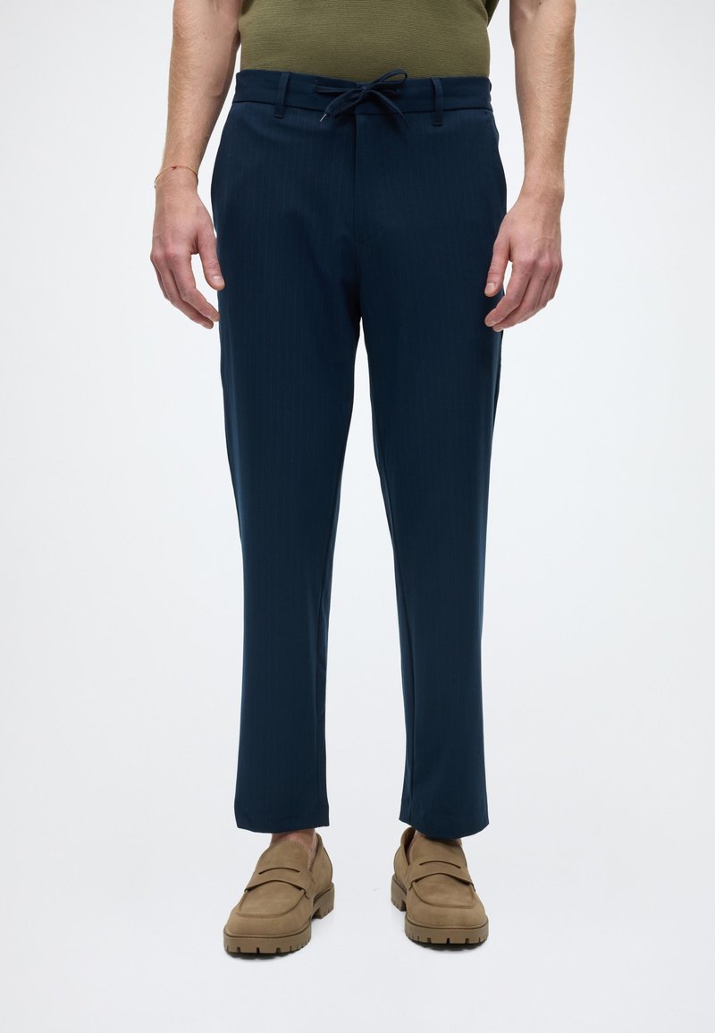 Pantalon bleu marine à rayures fines, fabriqué dans un tissu léger. Comprend une taille avec cordon de serrage et des jambes fuselées.