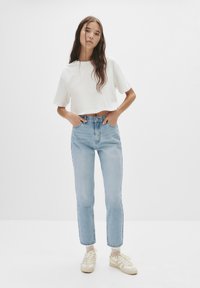 Fehér, rövidített póló, világoskék magasderekú farmer. A modell bézs tornacipőt visel. Egyszerű szabás, laza fazon, sima tapintás, minimális díszítés.