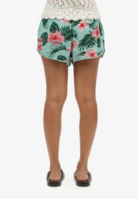 Shorts floraux en teal avec des motifs d'hibiscus roses et de feuilles de palmier vertes. Tissu doux, taille élastique et détail de bord festonné.