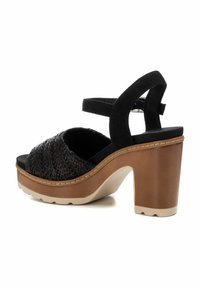 Sandalo platform intrecciato nero con tacco spesso marrone, cinturino alla caviglia regolabile e parte superiore in morbido tessuto. Presenta una suola beige a contrasto.