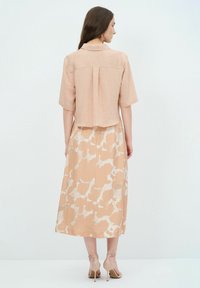 Kurzärmlige, hellpfirsichfarbene Bluse aus strukturiertem Stoff, kombiniert mit einem pastellfarbenen Rock mit floralem Muster in Beige- und Cremetönen. Offenes Rücken-Design.