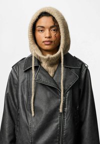 Jachetă din piele neagră cu accesorii argintii, suprapusă peste un hanorac bej, pufoasă, cu șnur și guler înalt. Textură netedă, design modern.