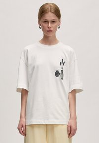 Witte katoenen t-shirt met een ontspannen pasvorm, uitgevoerd met zwarte geborduurde vazen en bladeren aan de linkerkant, korte mouwen en een ronde hals.