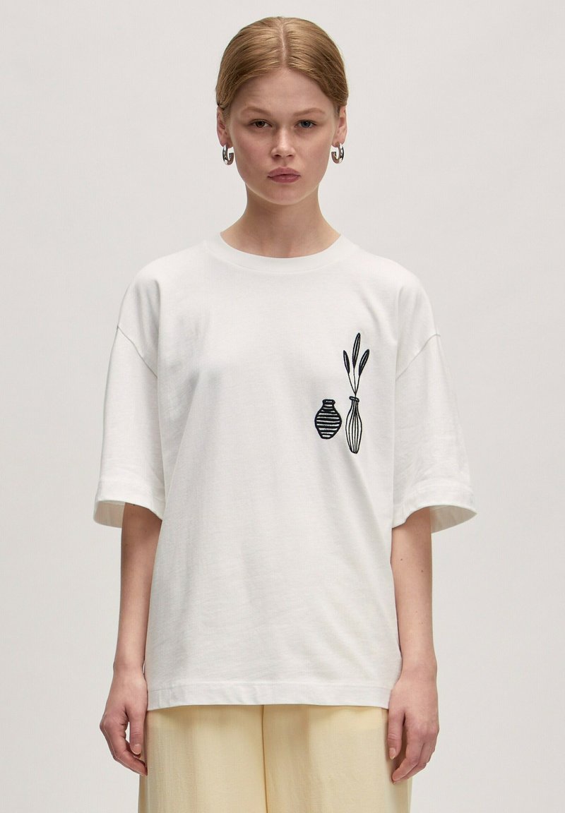 Witte katoenen t-shirt met een ontspannen pasvorm, uitgevoerd met zwarte geborduurde vazen en bladeren aan de linkerkant, korte mouwen en een ronde hals.