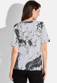 Kortemouwen top in zwart en wit, met een bloemenontwerp en stippen. De stof lijkt lichtgewicht met een gladde textuur.