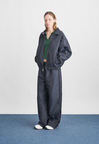 Fato de treino azul-marinho feito de tecido suave, apresentando uma jaqueta com fecho éclair, punhos elásticos e calças de corte descontraído. Combinado com sapatilhas brancas.