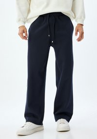 Pantalones de chándal navy con cintura elástica, cierre con cordones, bolsillos laterales y un corte relajado. Combinados con zapatillas blancas.