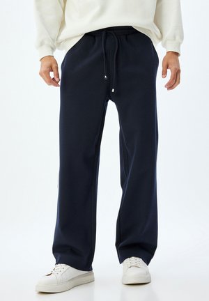 Marineblå sweatpants med elastisk talje, snorelukning, sidelommer og en afslappet pasform. Bæres med hvide sneakers.