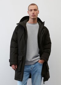 Schwarze isolierte Parkajacke mit Kapuze, Fronttaschen und Reißverschluss, über einem hellgrauen Pullover und blauen Jeans getragen. Glatte Stofftextur.