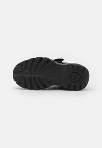 Black rubber shoe sole with textured tread pattern, featuring a rounded shape and a subtle logo imprint in the center.
