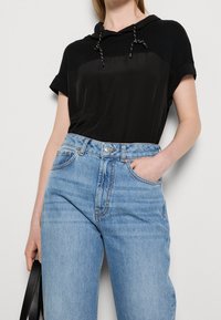 Sudadera corta negra de manga corta con cordones que se combina con jeans de tiro alto azul claro con un acabado desgastado y bolsillos frontales.