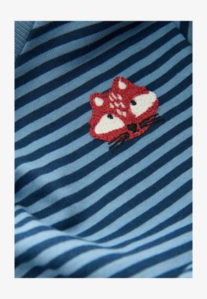 Kék és sötétkék csíkos ing, amelyen hímzett vörös róka minta található fehér kiegészítőkkel és fekete pofaszőrrel a mellrészen.