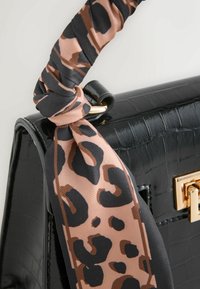 Sac à main noir en cuir de crocodile avec un marquage en relief et des finitions dorées, doté d'une anse en satin nouée au motif léopard noir et rose.