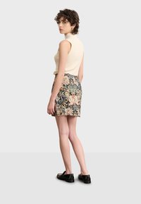Top sin mangas de punto en color crema combinado con una falda corta estampada con diseños florales en rosa, verde y negro, terminada con zapatos negros.