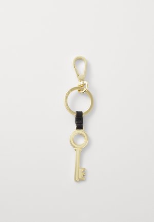 Portachiavi in metallo dorato con anello circolare, caratterizzato da un design a chiave scolpito. Un accentuazione in pelle nera collega la chiave all'anello.