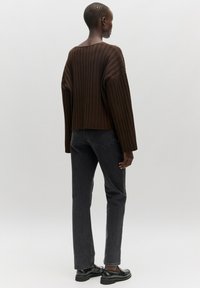 Brown ribbed sweater with wide sleeves, paired with high-waisted black jeans and black shoes, viewed from the back against a light background.