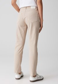 Licht beige denim broek met een slim fit, voorzien van twee achterzakken en een rechte pijpdesign. Gepaard met witte en grijze sneakers.