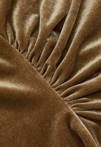 Barna bársonyszövet, amelynek egyik oldalán gyűrött textúra található, míg a másik oldalon sima felület, puha fényességgel és gazdag színmélységgel.