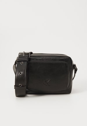 Bolso cruzado de cuero negro con un acabado texturizado, correa ajustable, bolsillo frontal con cremallera y logo en relieve. Forma rectangular compacta.